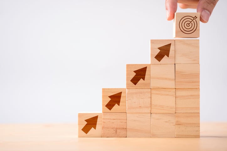 Stack of wooden blocks arranged as steps with arrows pointing upward, symbolizing growth, scalability, and achieving goals in incentive compensation management.