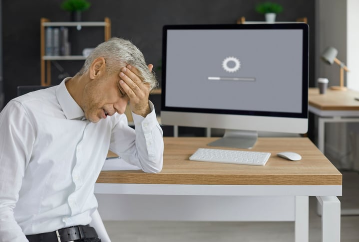 Frustrated business professional sitting at desk with computer showing loading screen, representing delays in ICM implementation