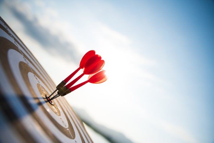 Three red darts hitting the bullseye on a target, symbolizing achieving company objectives and aligning goals with sales performance.