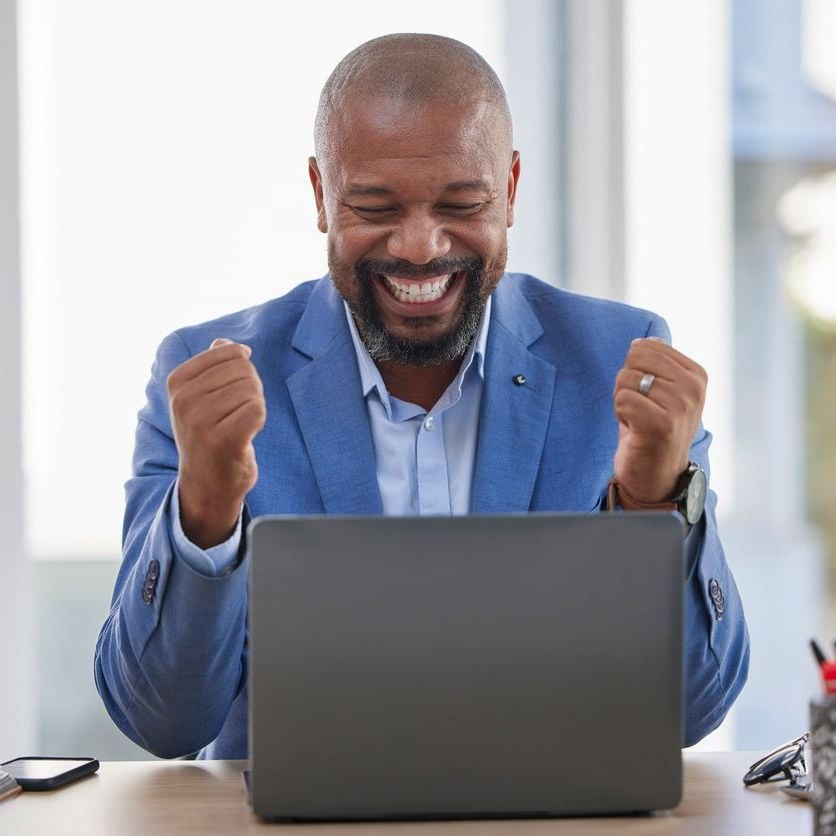 Sales representative celebrating incentive earnings while reviewing performance results on a laptop.
