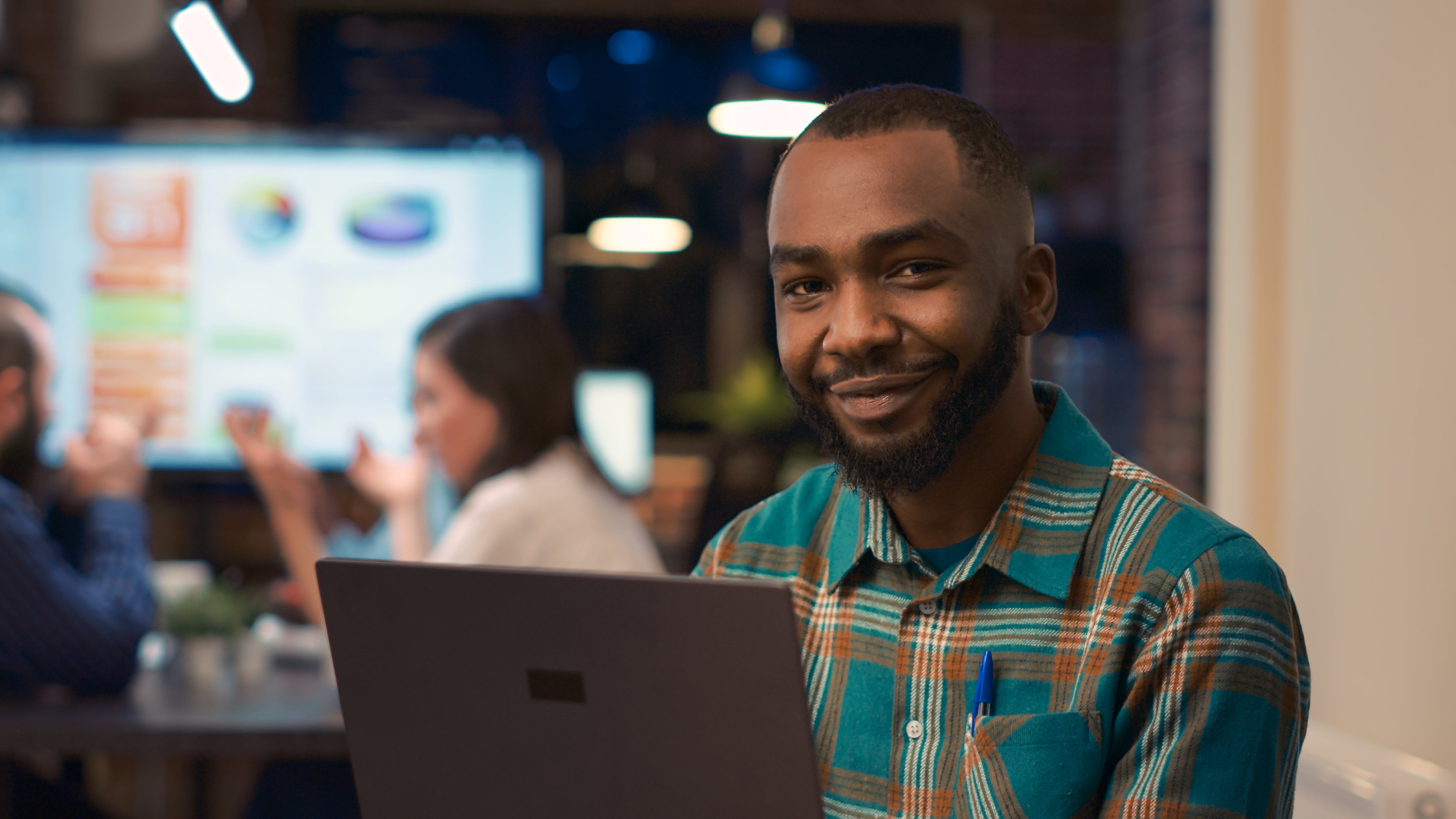 smiling-african-american-office-employee-working-laptop-portrait-young-man-holding-computer-looking-camera-close-up-company-financial-presentation-business-meeting-background-handheld-shot